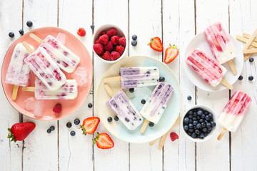 Sticker - Variety of homemade berry yogurt popsicles. Top view table scene on a rustic white wood background.