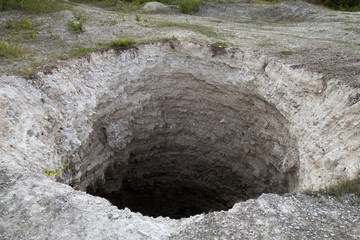 Black aperture of karst sinkhole, formed above abandoned limestone mine. Diameter about 15 ft, depth about 40-50 ft. Forming process is still going on