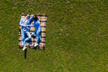 Wall Mural - Young couple in love lying on the grass looking up. Aerial view.