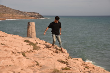 Young man walking next to a beautiful beach. Boy with a black t-shirt looking to the paradise, or maybe a desert. 