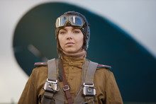 A Young Female Pilot In Uniform Of Soviet Army Pilots During The World War II. Military Shirt With Shoulder Straps Of A Major, Parachute, Flight Helmet And Goggles.