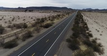 Tracking Cyclist Along Long Straight Road In Arizona With Deserted Landscape And Surrounding Mountains