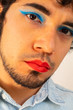 © Antonio Tanaka - Non-binary bearded young Hispanic man on a white background, with flamboyant makeup posing, red lips and blue eye shadows