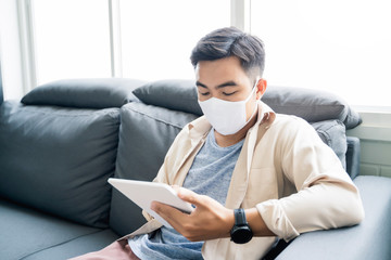 Fototapete - Working from home web designing graphical user interface UX UI, Asian man wearing protective mask using touching tablet device designing creative planning innovative idea, in living room quarantine