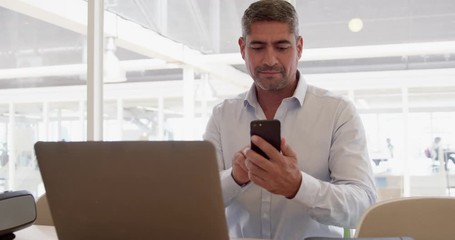 businessman using mobile phone while working on laptop in modern office
