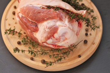 Pork meat.Raw meat with a bone with sprigs of thyme and peppercorns on a round  board on a black slate background.Texture pork raw meat close-up.