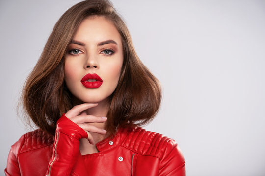 Portrait of beautiful young woman with bright makeup. Beautiful brunette with bright red lipstick on her lips. Pretty girl with long brown hair. Brunette dressed in a black leather jacket. Sexy girl