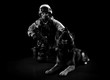 Armed man in military uniform sits next to a search dog