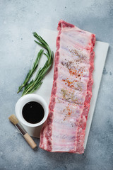 Wall Mural - Raw pork ribs with seasonings and bbq sauce, vertical shot on a light-blue stone background, top view