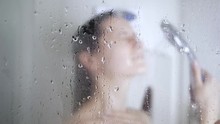 Attractive Caucasian Young Brunette Woman Taking Shower At Home Or At Hotel. Beautiful Girl Washing And Enjoy Herself Under Shower. Water Drops On Glass Door