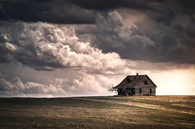 Old Wooden Farmhouse In The Countryside At Sunset With Storm  Clouds In The Sky. There Is A Short Grass Meadow Around The House.