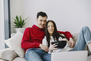 Cute couple in a bedroom. Lady in a white sweater. Pair watching film .