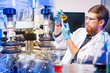 Results of a chemical experiment. A bearded man examines a yellow chemical in a flask. The chemist next to the distiller. Chemical laboratory equipment. Product quality control.