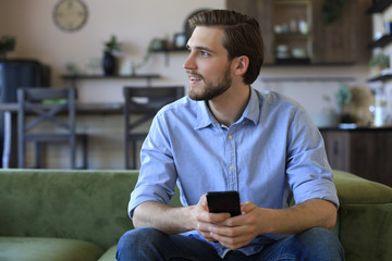 Attractive young man relaxing on a couch at home and using mobile phone for cheking social nets.