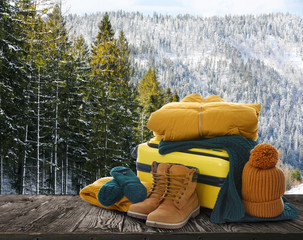 Sticker - Suitcase with warm clothes on wooden surface against beautiful winter landscape