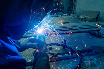 Poster - Metal welding. A worker in a protective helmet welds metal parts. Metalworking. Welding shop. Welding machine.