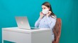 © Евгения Медведева - Female puts on a protective mask while working on a laptop in the workplace or at home during a pandemic. The concept of work during quarantine and self-isolation.