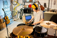 Young Musician In T-shirt And Beanie Hitting Drums And Cymbals With Drumsticks