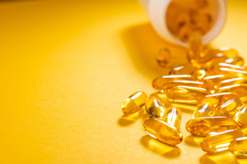 Yellow capsules scattered from a white bottle on orange background