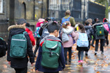 Fototapeta Londyn - Happy primary asian, india, Chinese & Caucasian student, kids, pupils & teacher carrying  school bags on their way to visit British museum, London, in rain winter day, with red maple leaves on ground