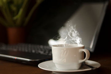 A cup of coffee on the working table near a laptop