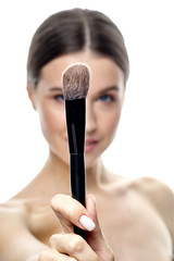 close-up portrait of a young brunette girl with blue eyes with clear skin, doing makeup with makeup brushes, isolated on a white background. High-resolution photos