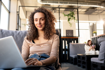 Poster - Pretty young female with dark wavy hair looking at you while sitting on couch