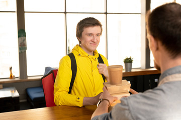 Poster - Happy young courier with big backpack looking at waiter by counter