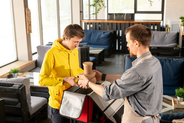 Aufkleber - Young waiter helping courier with packing backpack in restaurant