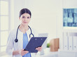© lenets_tan - Young smiling female doctor with stethoscope holding a folder at doctor's office