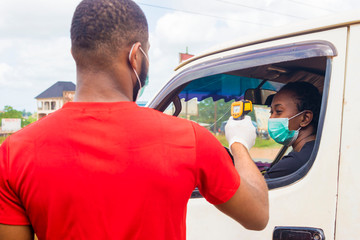 Wall Mural - young black man wearing a nose mask, checking the temperature of a black woman driving a car