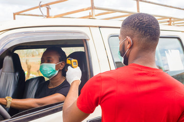 Wall Mural - young black man wearing a nose mask, checking the temperature of a black woman driving a car