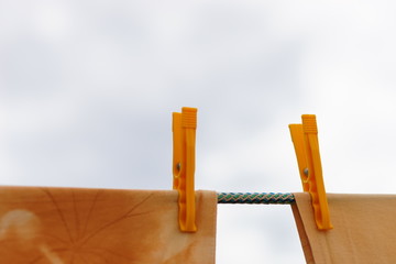 Beige clothes are dried with yellow plastic clothespins outdoors.