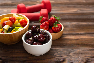 Wall Mural - Healthy foods  Concept ,blueberry  strawberry apple  with salad  in  bowl  dumbbells on white wood background