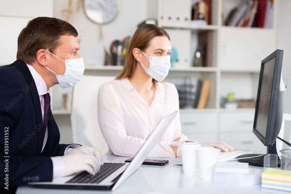 Entrepreneur in medical mask working with female coworker in office - obrazy, fototapety, plakaty 