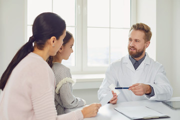 Wall Mural - Male doctor gives mom and daughter a prescription while sitting at a table in a clinic office.