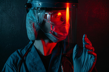 Wall Mural - female doctor with a stethoscope on her neck, in a medical mask and glasses on her face on a dark background