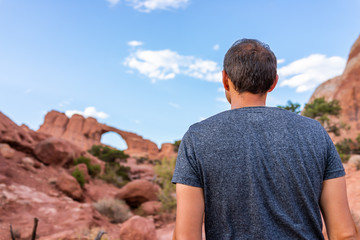 Wall Mural - Arches National Park with Skyline Arch canyon in background and back of young man standing looking at view on trail hike in Utah