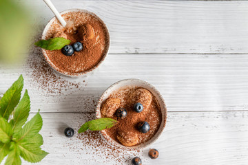 Wall Mural - Top view of tiramisu dessert with blueberries, mint in white jar on grey background. Flat lay concept. Copy space.