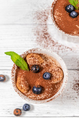 Wall Mural - Classic tiramisu dessert with blueberries, mint in white jar on grey background. Flat lay concept. Vertical