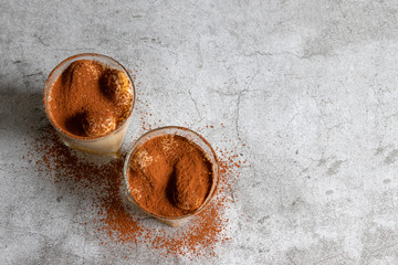 Wall Mural - Top view of traditional Italian sweet tiramisu cake dessert in glass on grey background. Copy space.