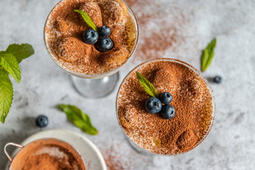 Wall Mural - Close up of traditional Italian sweet tiramisu cake dessert with mint and blueberry berries in glass on grey