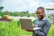 © Confidence - young african agricultural businessman, using a laptop on a plot of land