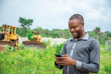 african agricultural businessman, using a mobile phone on a plot of land