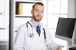 © rogerphoto - Friendly red-bearded doctor sitting and writing at clipboard in clinic. Perfect medical service in hospital. Medicine concept