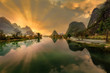 Dramatic shot of the sun rising behind limestone karst mountains in Yangshuo County with the scene reflected in the river