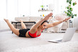 © Admiral - Fit woman doing superman's exercise and watching online workout tutorial on laptop, training in living room