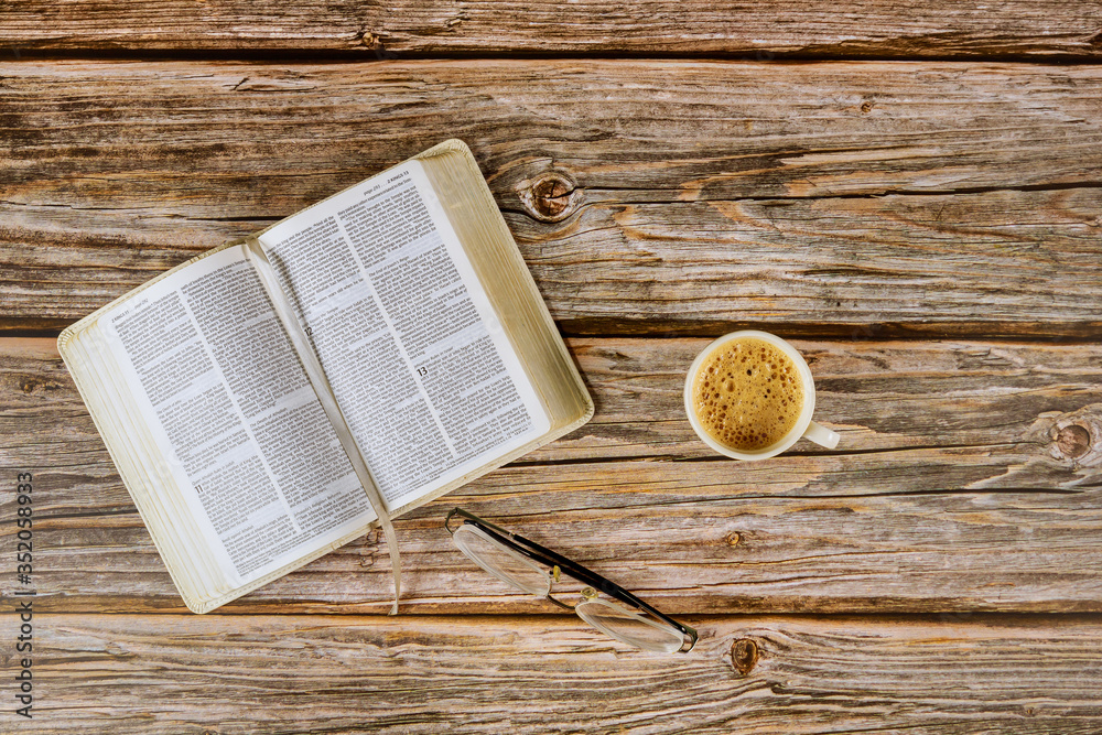Open Bible morning readings on a table top with coffee cup and eyeglasses - obrazy, fototapety, plakaty 