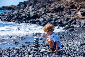 The collapse of hopes and plans. Harmony and emotions. A boy is playing with a stone tower on the ocean. Destroy a tower of stones.