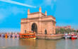 The Gateway of India and boats as seen from the Harbour - Mumbai, India - Trail of white smoke from the airplane on blue sky
